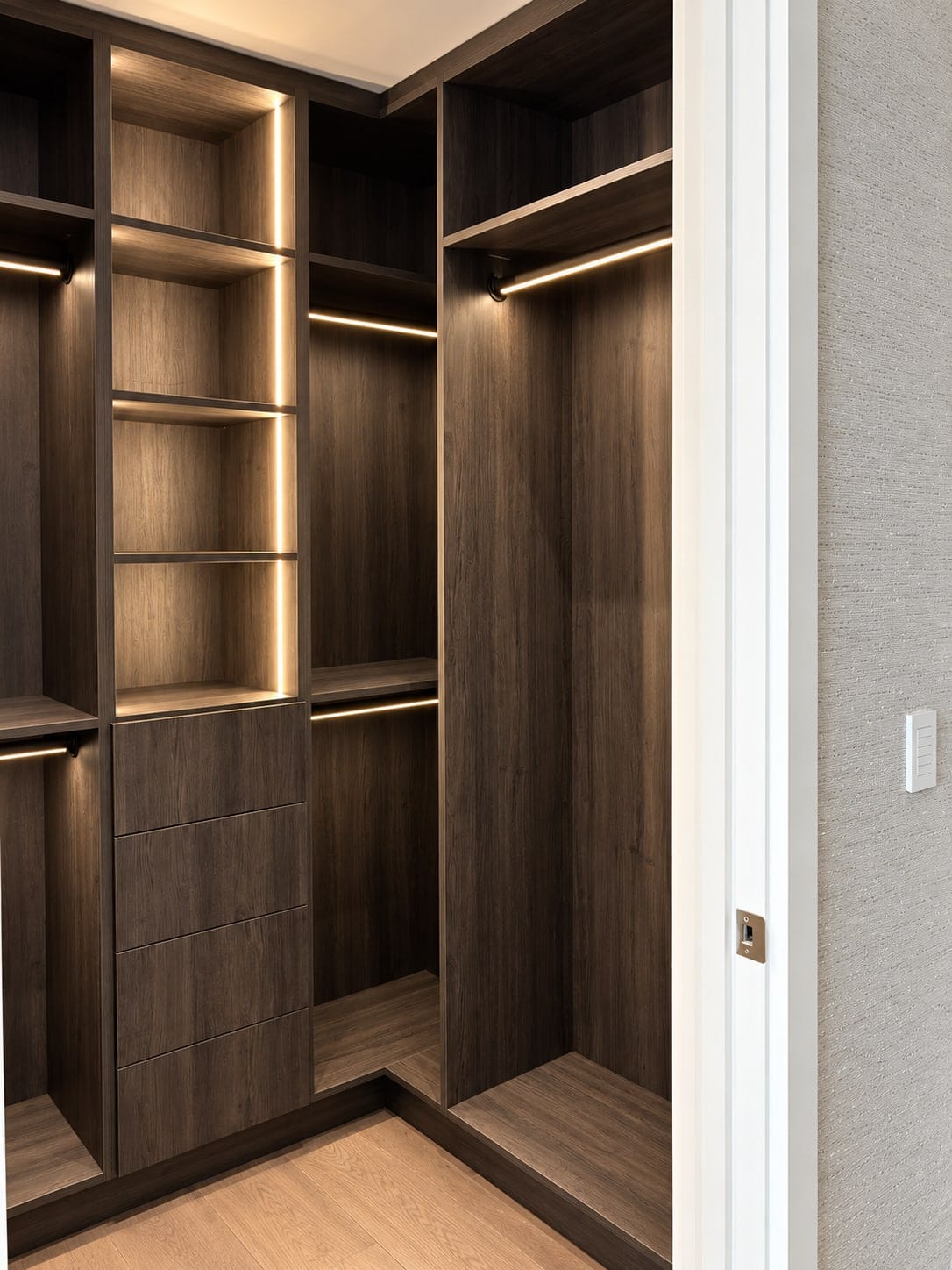 Dark wood corner closet with lit shelves and hanging rails