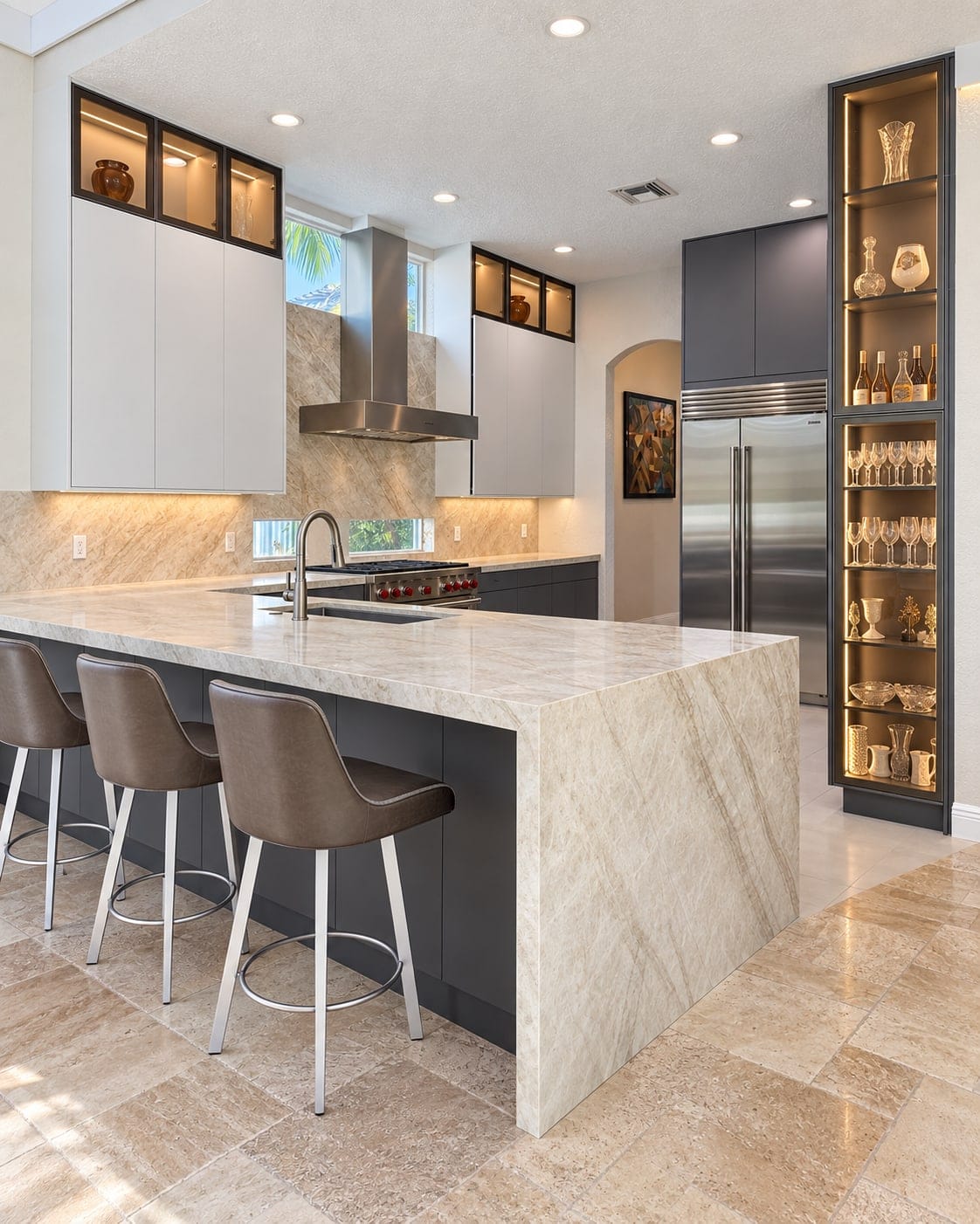 Kitchen with a waterfall island, graphite cabinetry and a lit glass display column